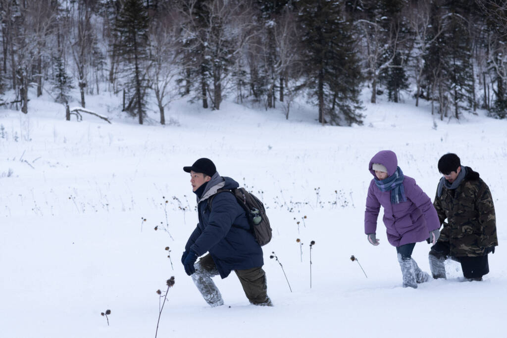 A man and two children walk through thick snow in the woods.